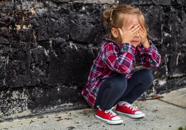 Young girl crouching next to wall
